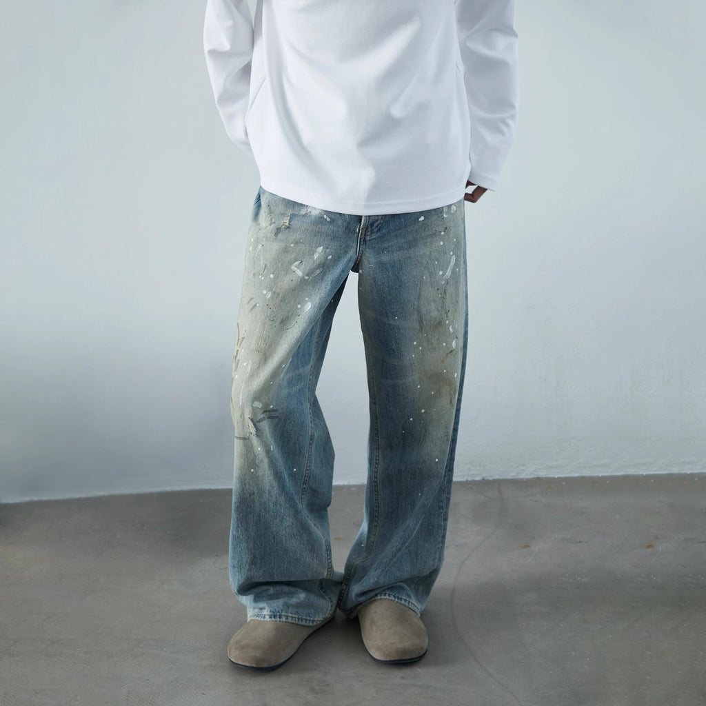 Calça jeans neutra de perna larga com estampa desgastada de respingos de tinta.
